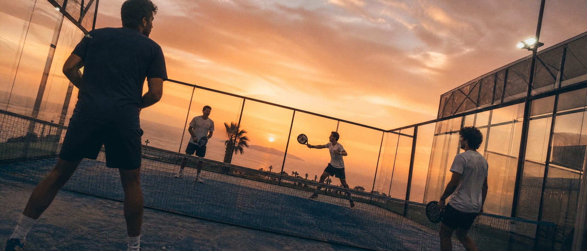 Cuatro amigos jugando pádel al atardecer frente al mar
